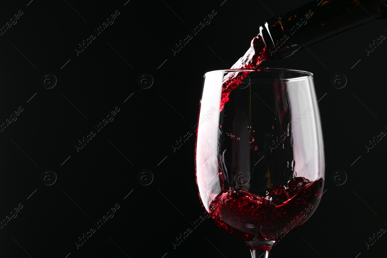 Photo of Pouring red wine into glass against black background, closeup. Space for text