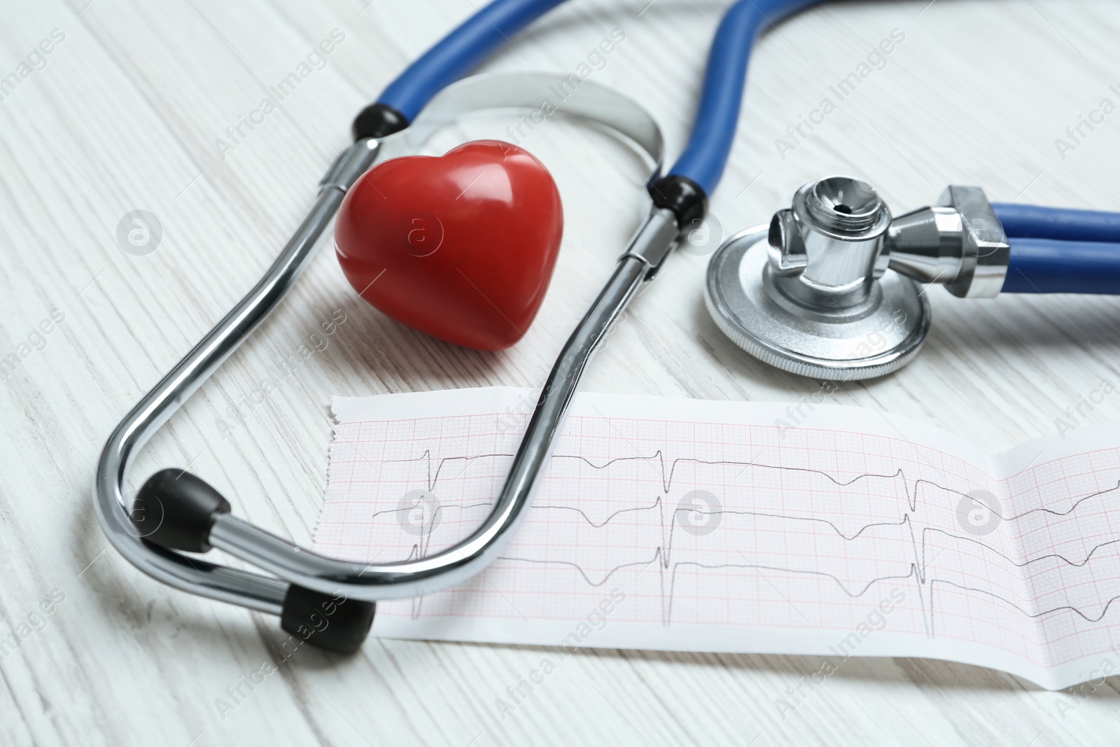 Photo of Cardiogram report, red heart and stethoscope on white wooden table