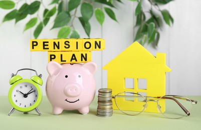 Photo of Yellow cubes with phrase Pension Plan, piggy bank, stack of coins and alarm clock on light green table. Retirement concept