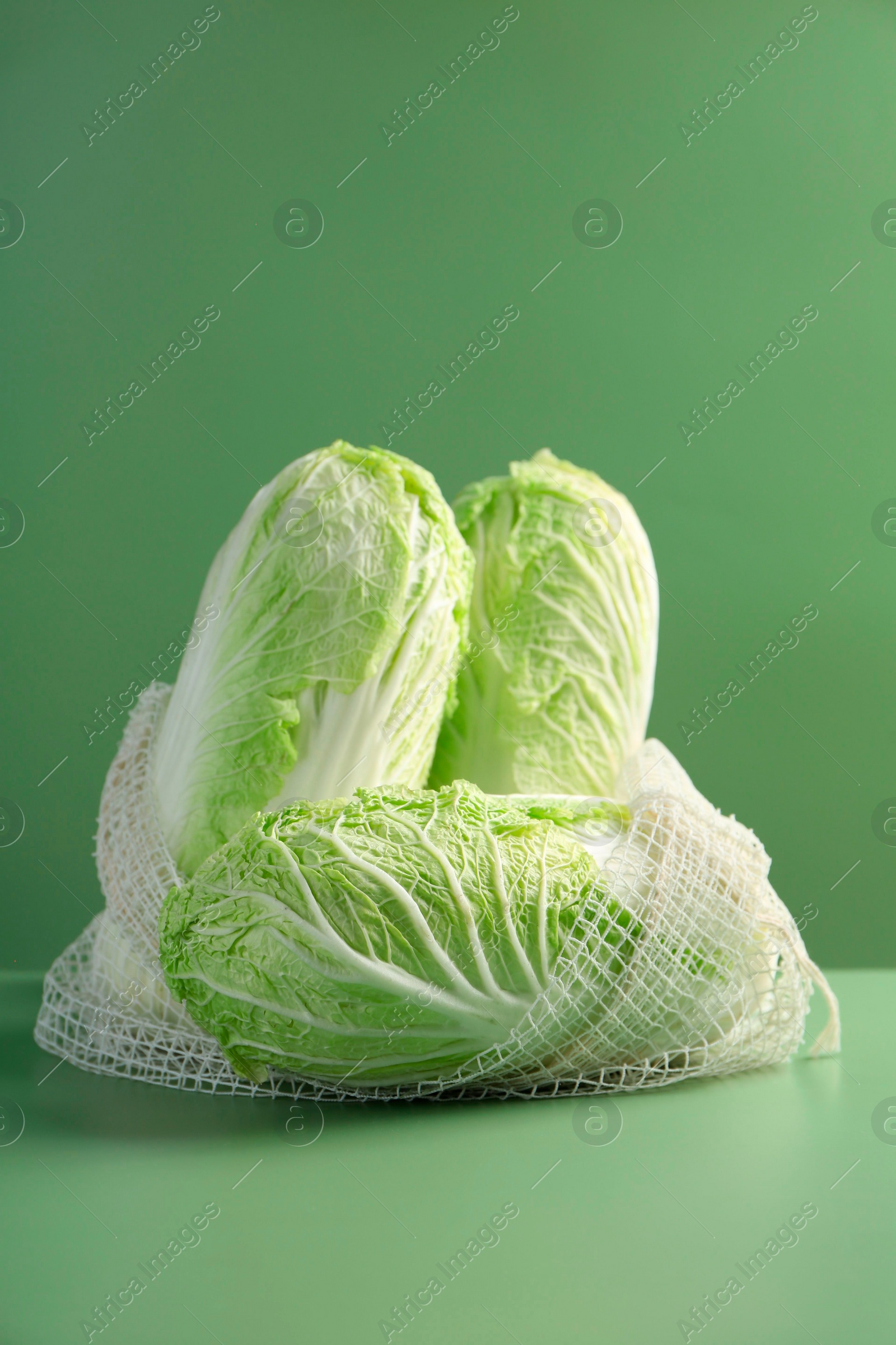 Photo of Fresh Chinese cabbages in string bag on green background