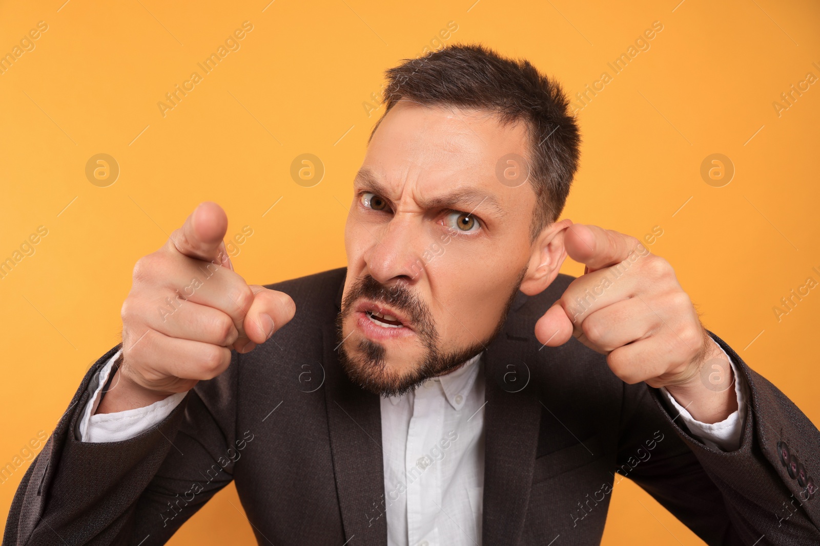 Photo of Aggressive man pointing on orange background. Hate concept