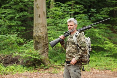 Photo of Man with hunting rifle wearing camouflage in forest. Space for text