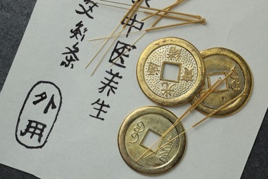 Photo of Acupuncture needles, Chinese coins and paper with characters on table, flat lay