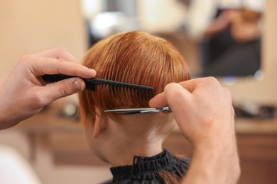 Professional hairdresser cutting boy's hair in beauty salon, closeup