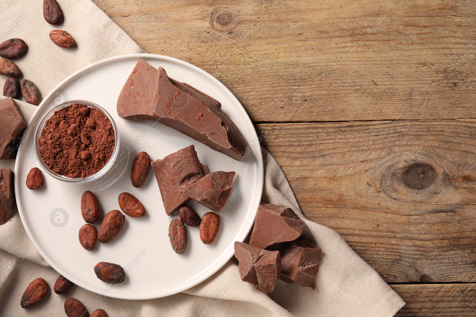 Photo of Pieces of tasty milk chocolate, cocoa beans and powder on wooden table, top view. Space for text