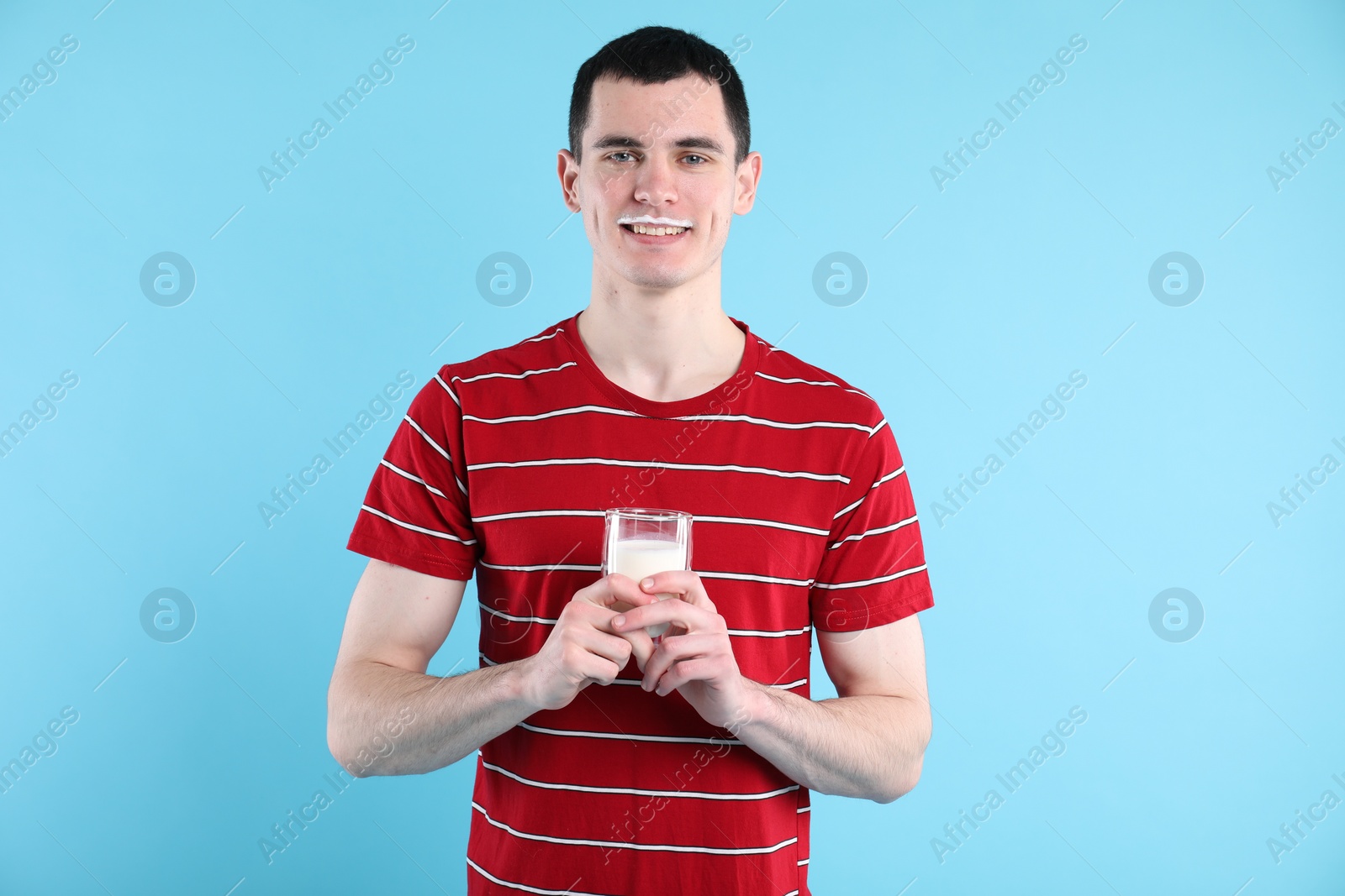 Photo of Happy man with milk mustache holding glass of tasty dairy drink on light blue background