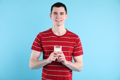 Happy man with milk mustache holding glass of tasty dairy drink on light blue background