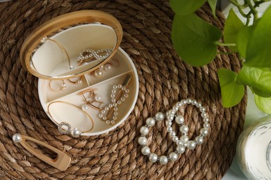 Stylish jewelry with pearls and box on wicker mat, flat lay