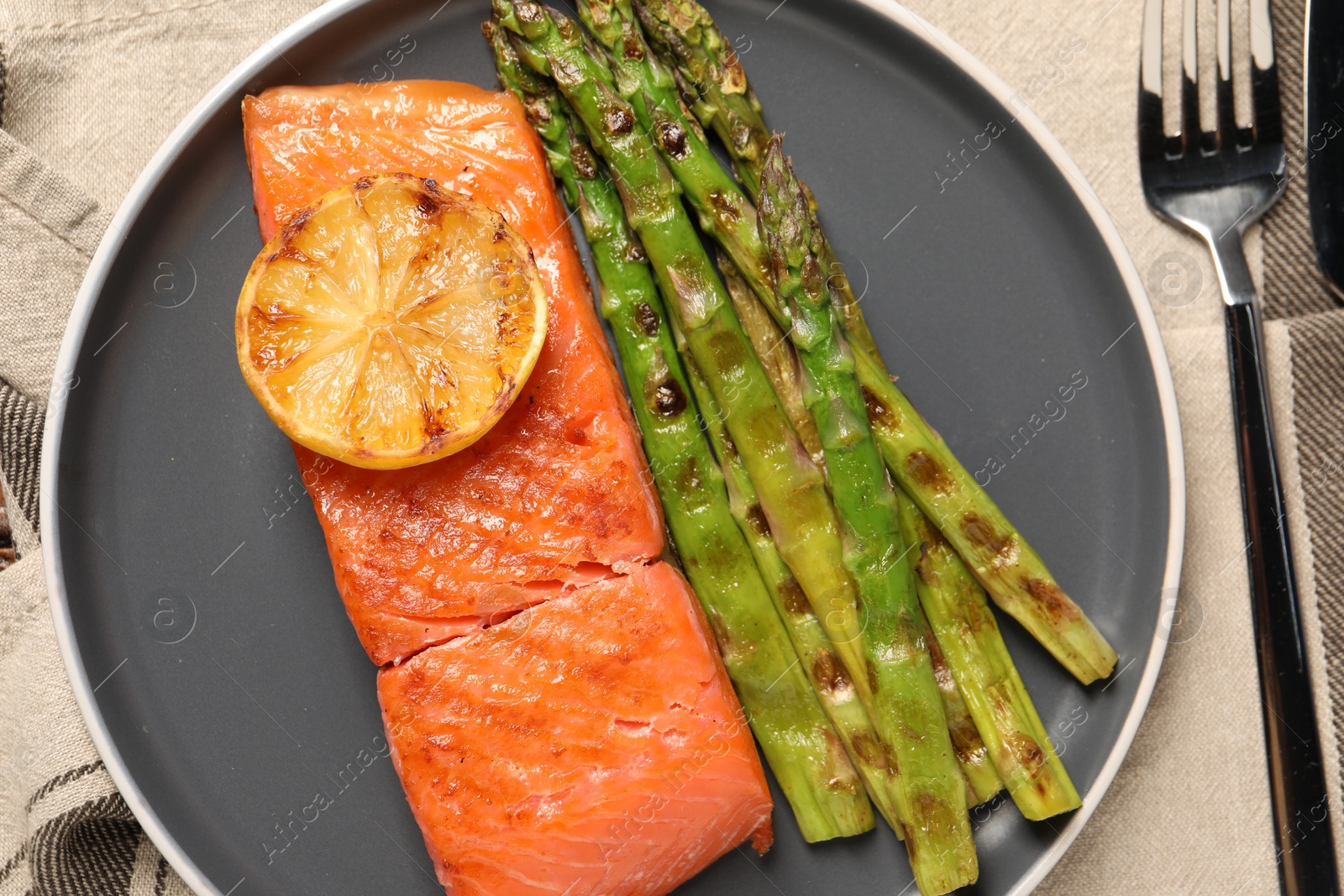 Photo of Tasty grilled salmon with asparagus and lemon served on tablecloth, flat lay