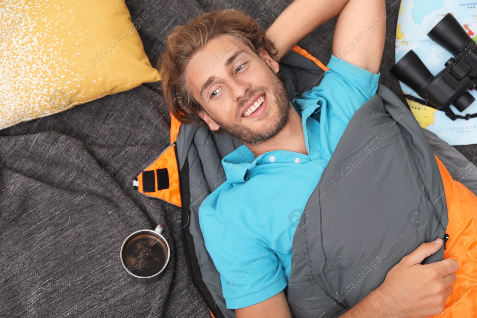 Photo of Young man in comfortable sleeping bag on blanket, top view