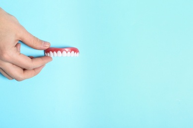 Photo of Woman holding teeth cover on color background, top view. Space for text