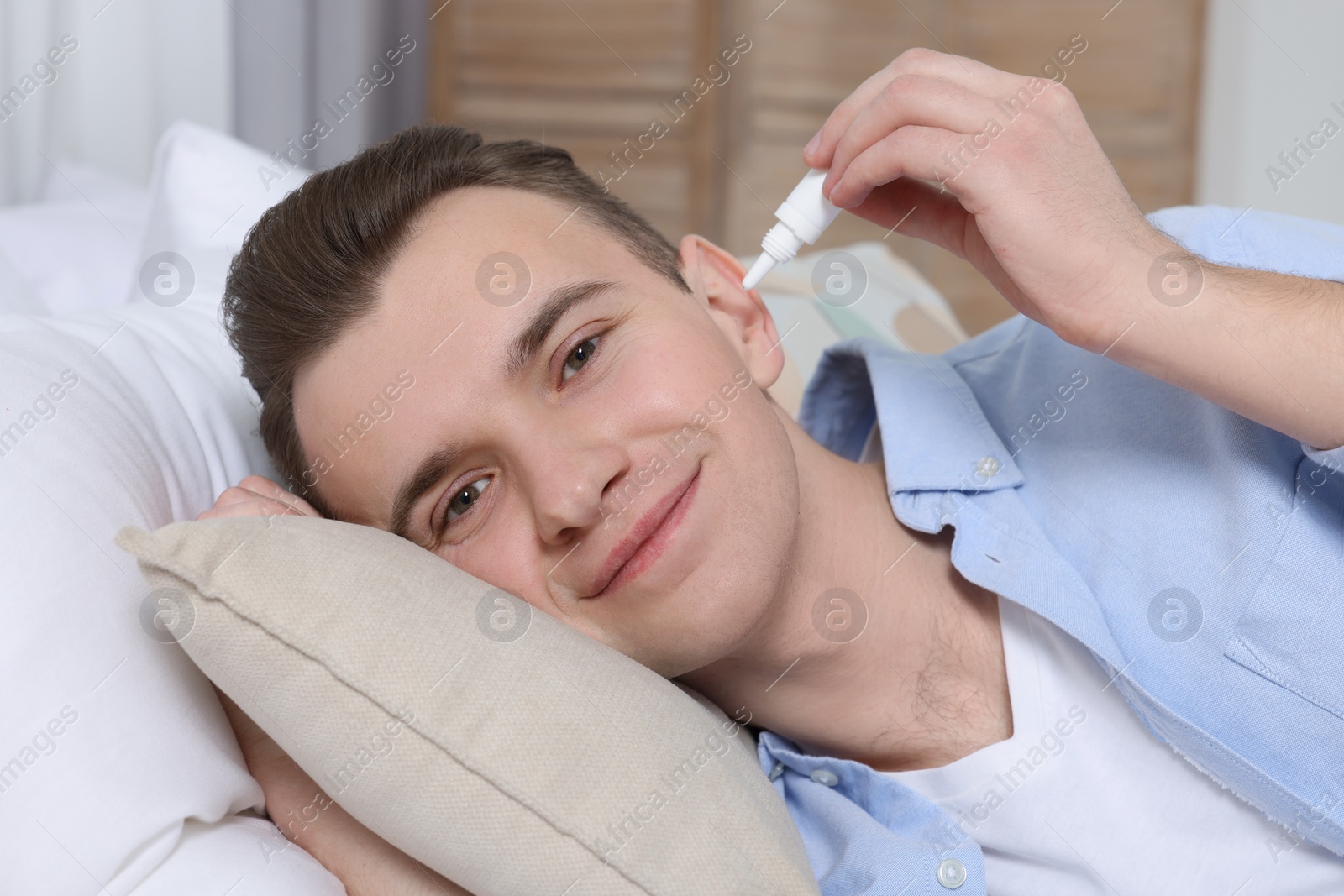 Photo of Young man using ear drops at home