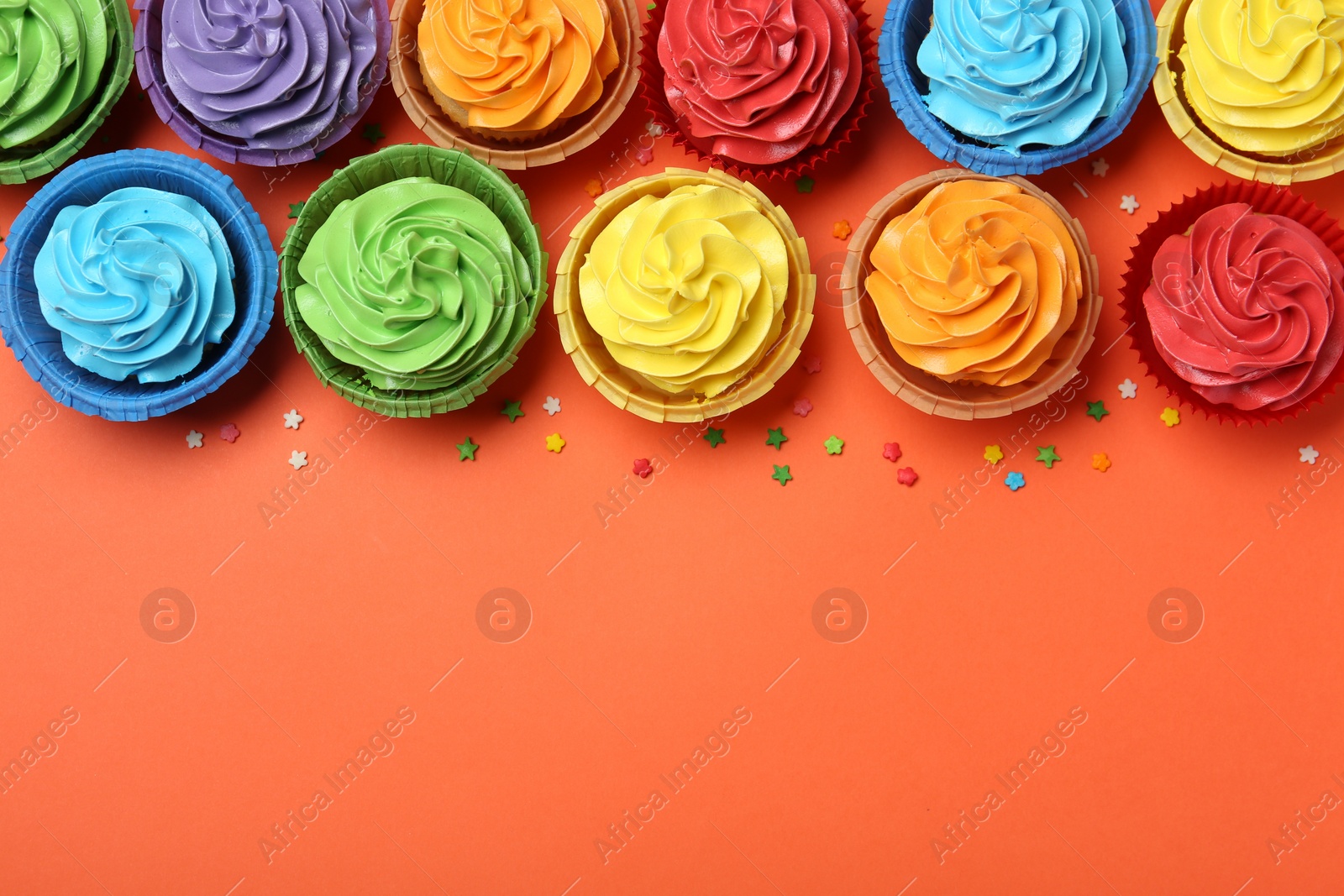 Photo of Delicious bright cupcakes and sprinkles on coral background, flat lay. Space for text