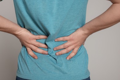 Man suffering from back pain on light grey background, closeup. Arthritis symptoms