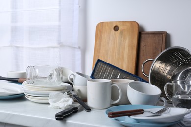 Many dirty utensils and dishware on countertop in messy kitchen