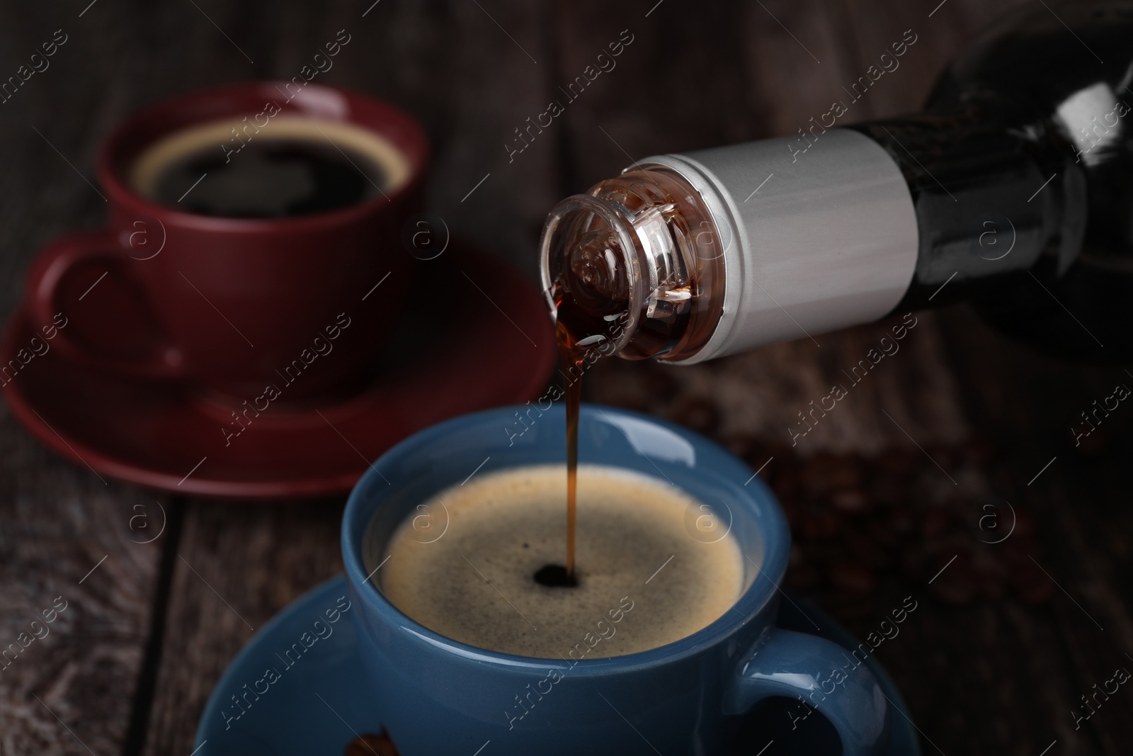 Photo of Pouring delicious syrup into cup with coffee at wooden table, closeup