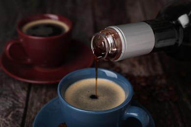 Photo of Pouring delicious syrup into cup with coffee at wooden table, closeup