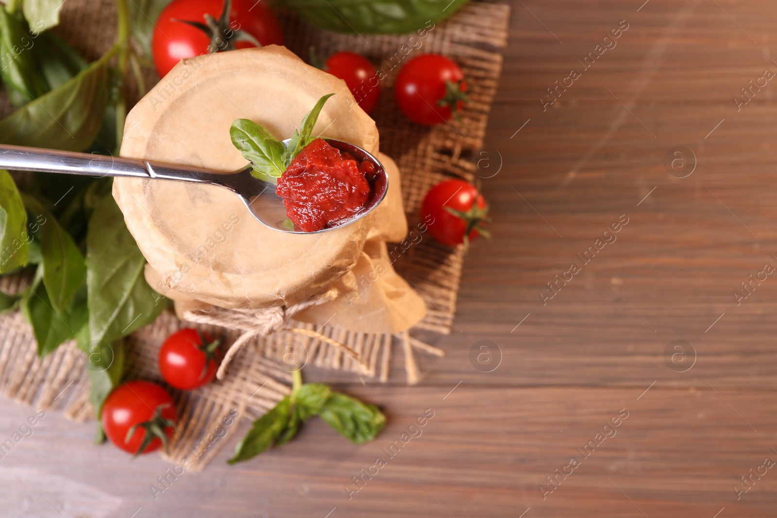 Photo of Jar of tasty tomato paste with spoon and ingredients on wooden table, flat lay. Space for text