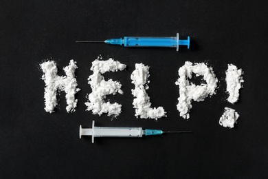 Photo of Text Help written with cocaine powder and syringes on black background, top view