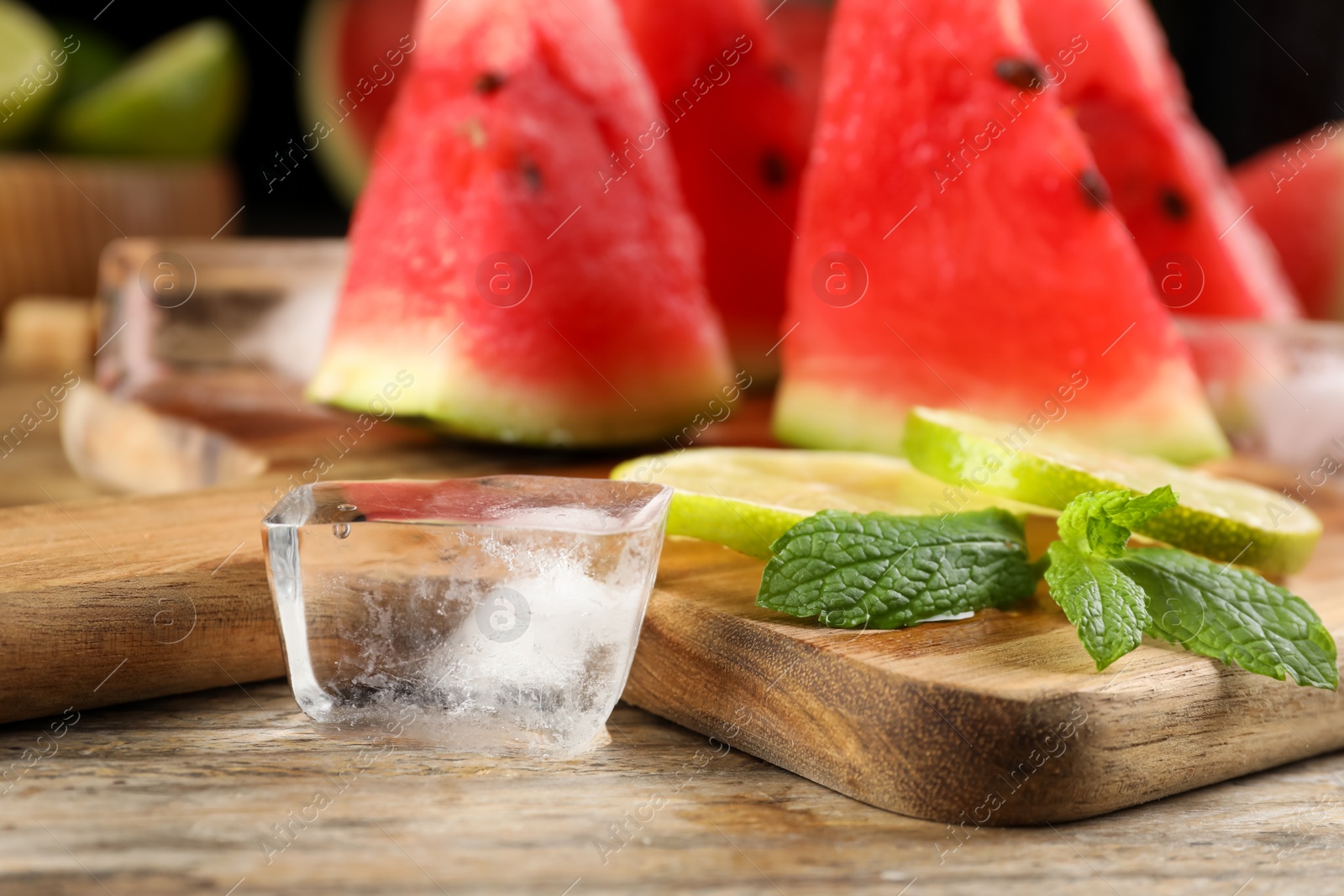 Photo of Board with ice, juicy watermelon and lime slices on wooden table, closeup