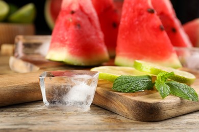 Photo of Board with ice, juicy watermelon and lime slices on wooden table, closeup