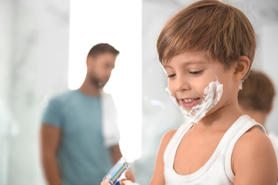 Happy little boy with shaving foam on face in bathroom, space for text. Dad and son having fun