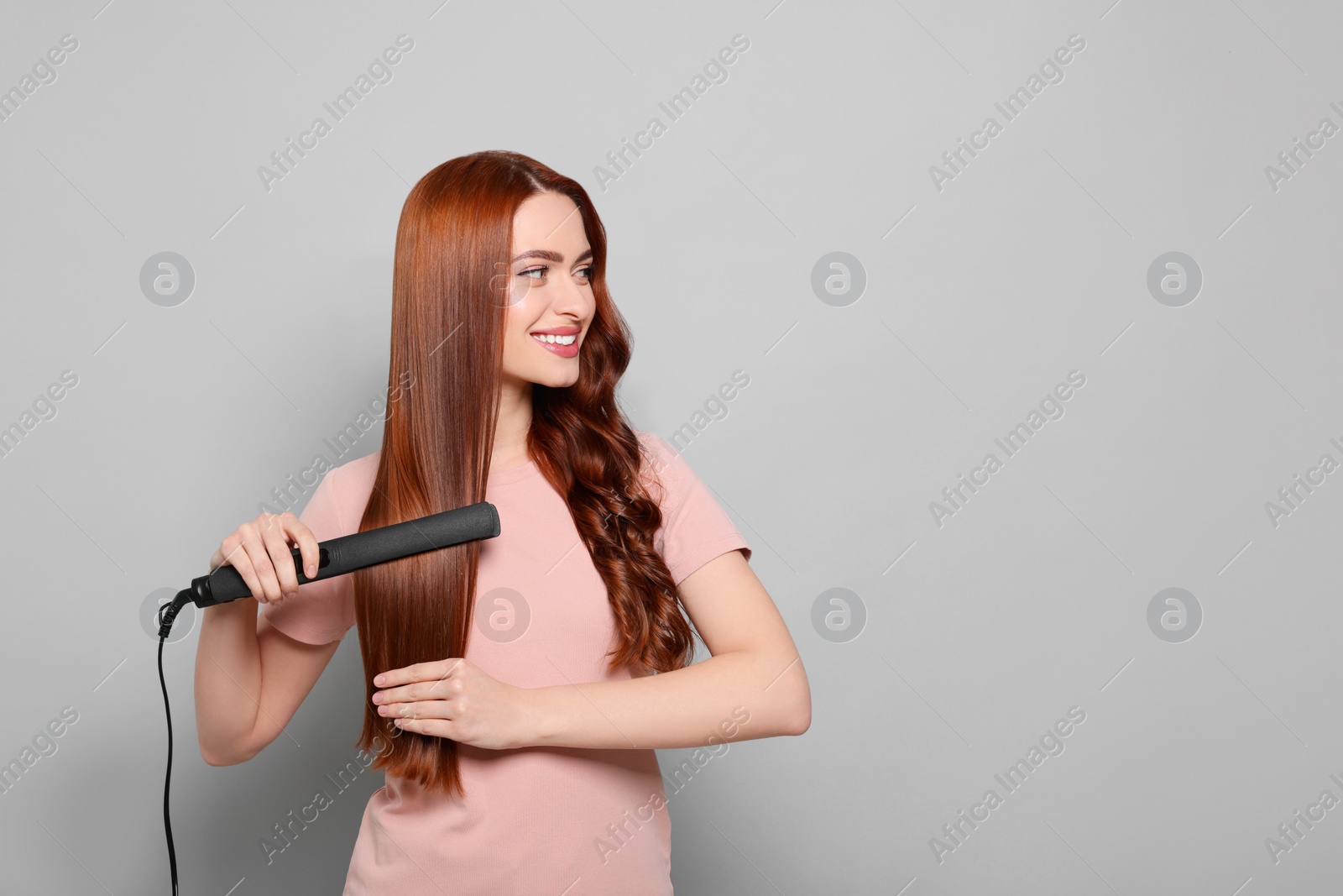 Photo of Beautiful woman using hair iron on light gray background, space for text