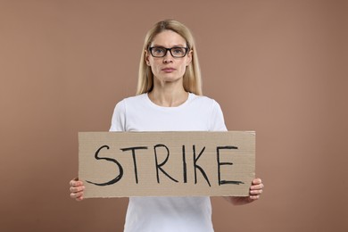 Woman holding cardboard banner with word Strike on brown background