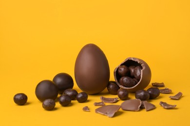 Tasty whole and broken chocolate eggs with candies on orange background