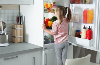 Cute girl taking apple out of refrigerator in kitchen