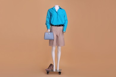Photo of Female mannequin dressed in leather shorts, light blue shirt with accessories and shoes on beige background. Stylish outfit