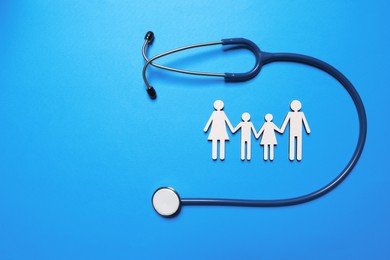 Figures of family near stethoscope on light blue background, flat lay. Space for text. Insurance concept