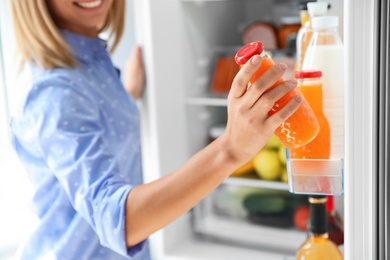 Photo of Woman taking bottle with juice out of refrigerator in kitchen