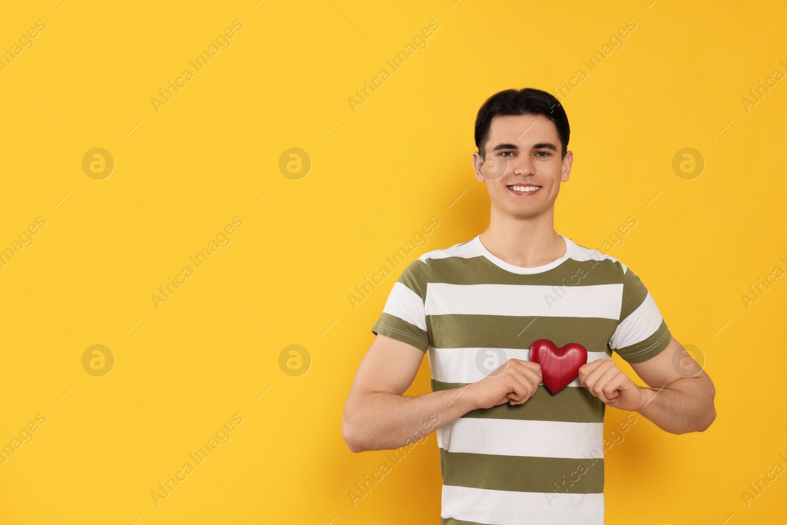 Photo of Happy volunteer holding red heart with hands on orange background. Space for text