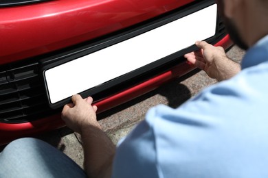 Photo of Man installing vehicle registration plate outdoors, closeup. Mockup for design