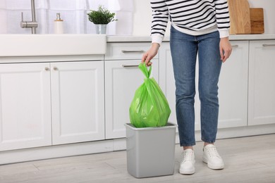 Photo of Woman taking garbage bag out of trash bin in kitchen, closeup. Space for text