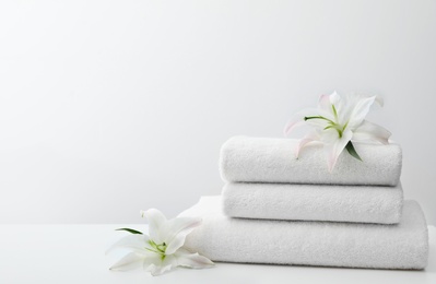 Stack of fresh towels with flowers on table against white background. Space for text