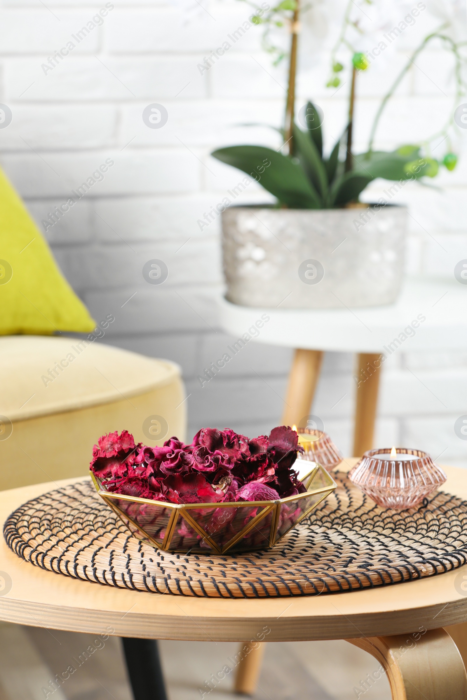 Photo of Aromatic potpourri of dried flowers in bowl and burning candles on wooden table indoors