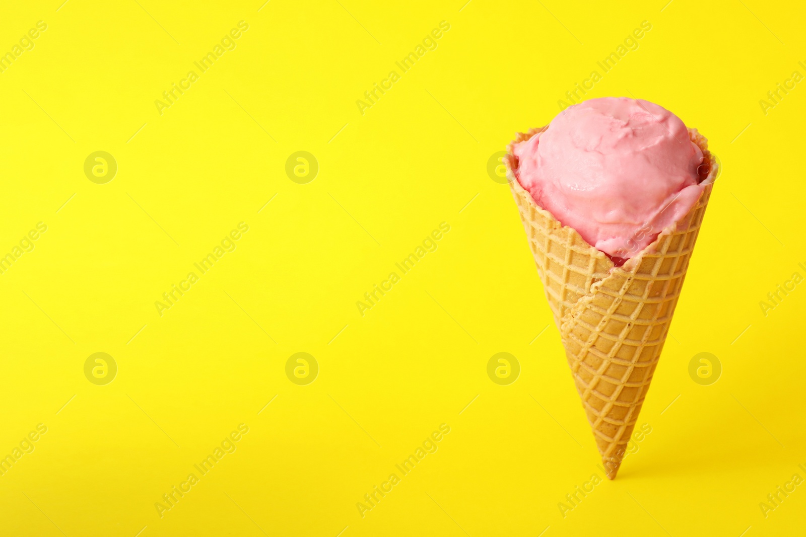 Photo of Delicious pink ice cream in waffle cone on yellow background. Space for text