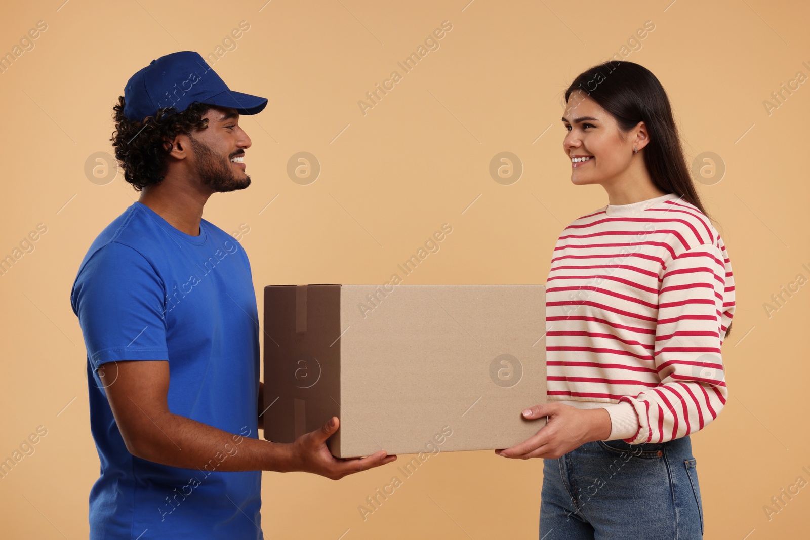 Photo of Smiling courier giving parcel to receiver on light brown background