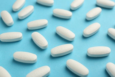 Photo of Vitamin pills on light blue background, closeup