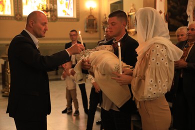 Photo of Stryi, Ukraine - September 11, 2022: Parents holding child and candles during baptism ceremony in Assumption of Blessed Virgin Mary cathedral
