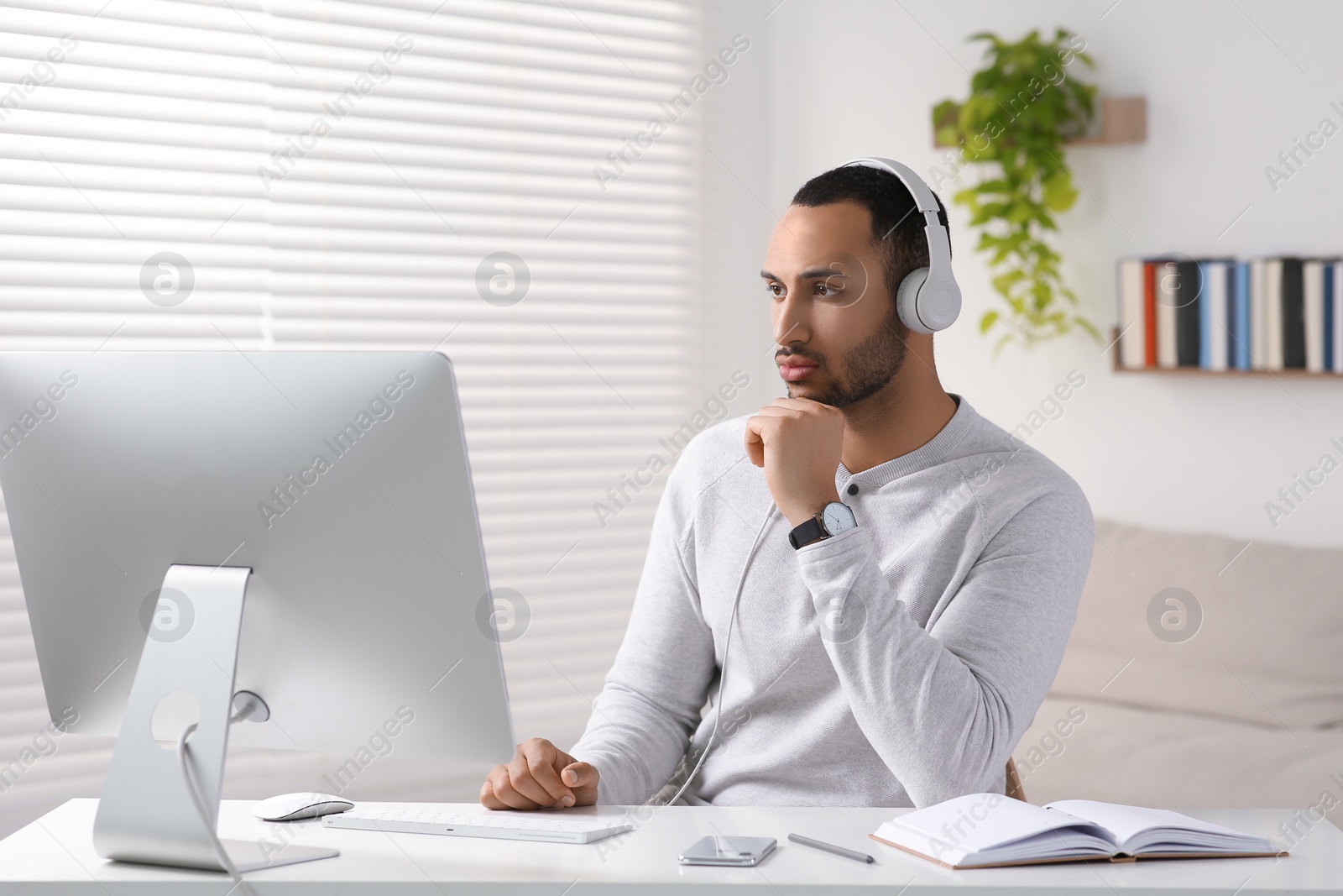 Photo of Young man with headphones working on computer at desk in room. Home office