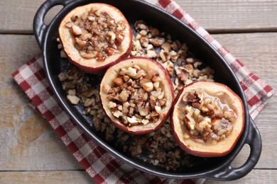 Tasty baked apples with nuts and honey in baking dish on wooden table, top view