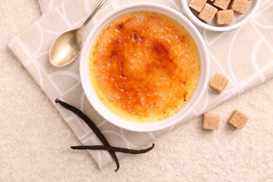 Photo of Delicious creme brulee in bowl, vanilla pods, sugar cubes and spoon on light textured table, top view