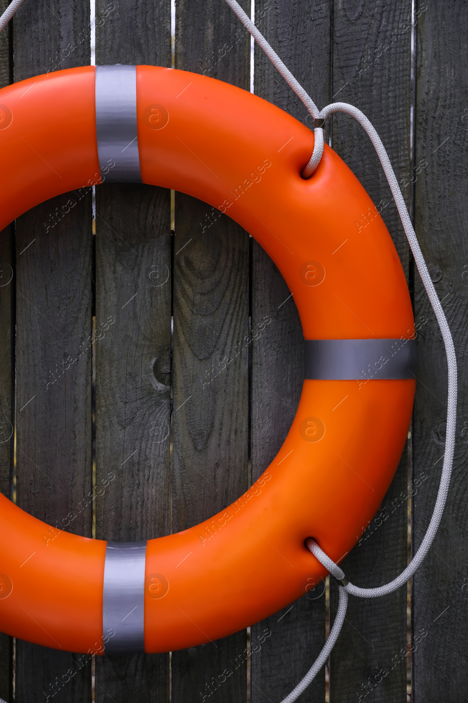 Photo of Orange lifebuoy hanging on grey wooden fence. Rescue equipment