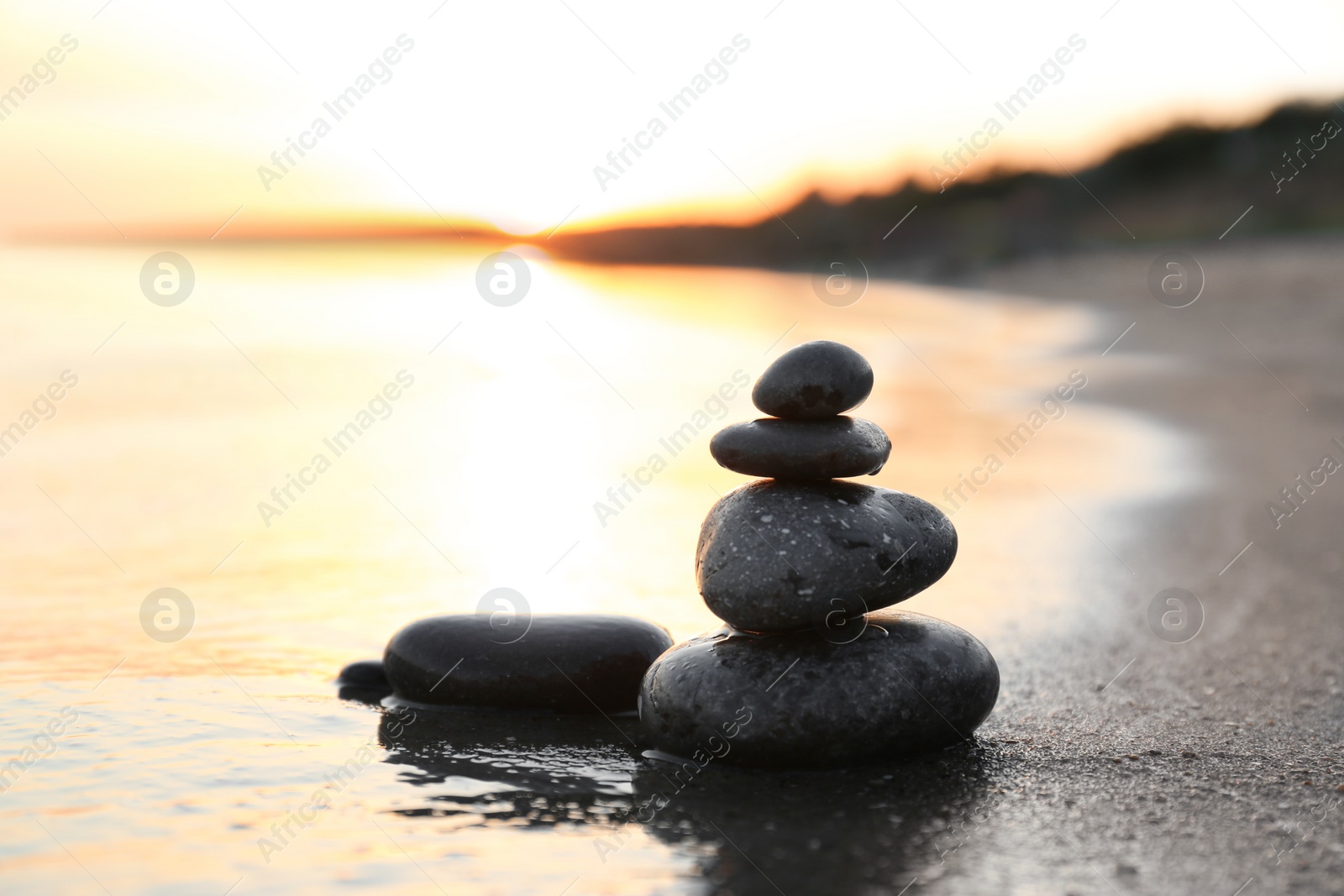 Photo of Dark stones on sand near sea at sunset, space for text. Zen concept