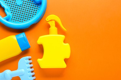 Bottles of suntan cream and children's beach toys on orange background, flat lay. Space for text