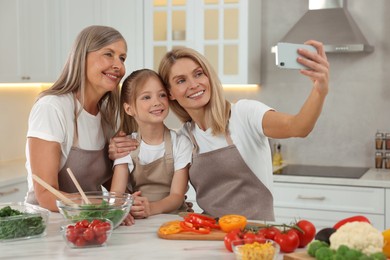 Photo of Three generations. Happy grandmother, her daughter and granddaughter taking selfie while cooking together in kitchen