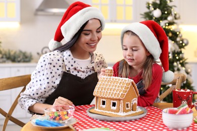 Mother and daughter decorating gingerbread house at table indoors